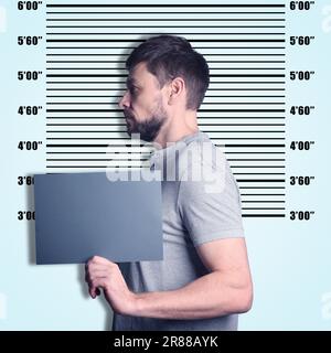 Criminal mugshot. Arrested man with blank card against height chart Stock Photo