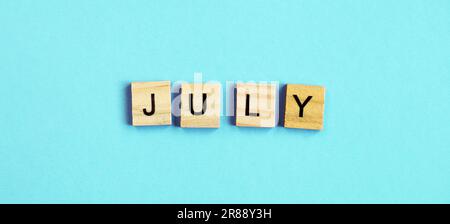 July word made by wooden cubes on a blue turquoise background. Stock Photo