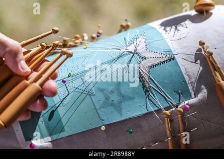Hands of a woman making a bobbin lace star shape with threads on wooden bobbins and pins in the pattern on the lace pillow, detail shot, selected focu Stock Photo
