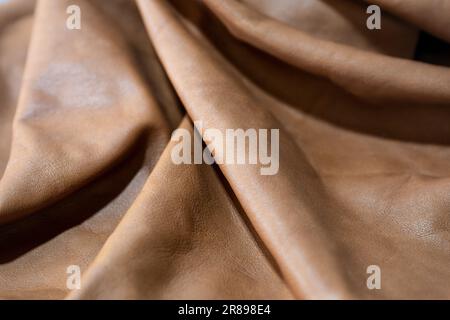 Soft brown leather laying in waves, used for furniture, bags or clothing in a craft workshop, full frame background, copy space, selected focus, narro Stock Photo