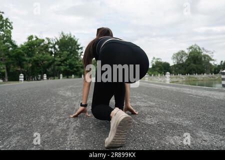 Sportive woman outdoors. Young lady doing exercises and ready to start running. Health and sport concept Stock Photo