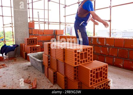 Heap of red blocks waiting to be installed, in background mason is ...