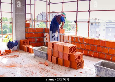 Heap of red blocks waiting to be installed, in background mason is ...