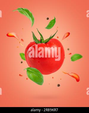 Flying tomato with splashes and basil leaves on red background. Stock Photo