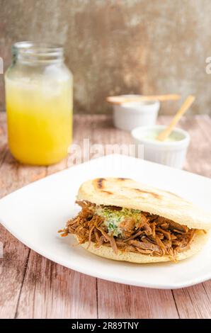 Traditional Venezuelan arepa accompanied by guasacas. Rustic and wooden background Stock Photo