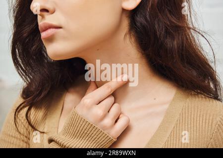 Cropped view of young brunette woman doing self-massage of thyroid gland on neck and lymphatic circulation at home, self-care ritual and holistic well Stock Photo