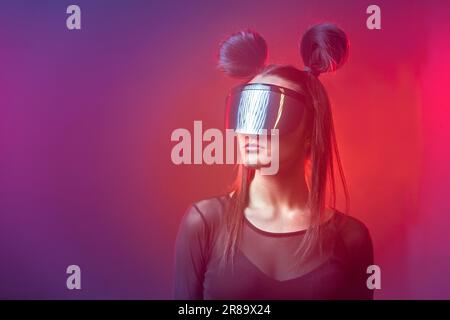 Portrait of beautiful cyber model woman posing wearing futuristic glasses on head with neon light in a virtual tech environment Stock Photo