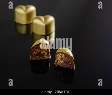 Chocolate bonbon in the shape of a golden heart cut in half. plain black background Stock Photo