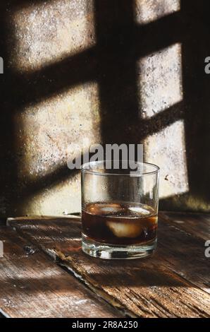 Brandy glass on rustic background and rustic wooden table. Shadows in background. Stock Photo