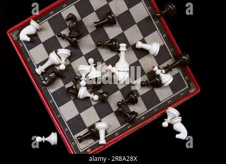 Little plastic chess pieces lying chaotically on a black and white chessboard. Portable travel mini game. Chess figures scattered on a board Stock Photo