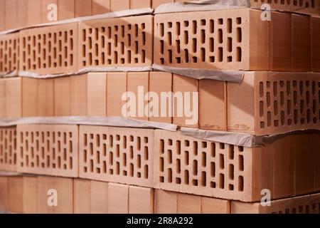 Many new hollow bricks stacked in a warehouse for sale. Lots of orange clay bricks at a construction site Stock Photo