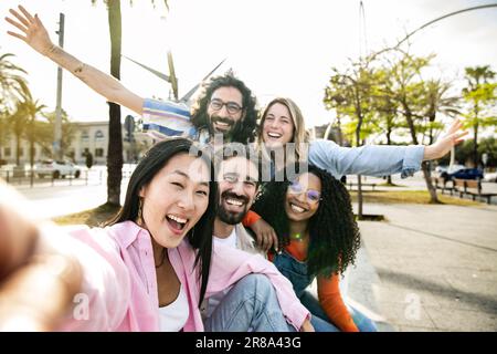 Multi ethnic group of millennial friends taking a selfie in the street. Cheerful multiracial group of young hipsters laughing and taking a picture Stock Photo