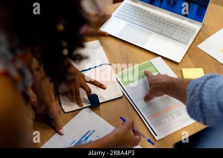 High angle view of diverse colleagues using laptop and documents in casual office meeting Stock Photo
