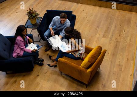 High angle view of diverse male and female colleagues in discussion using laptop in office lounge Stock Photo