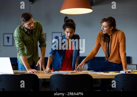 Focused diverse male and female colleagues using laptop and notes in casual office meeting Stock Photo