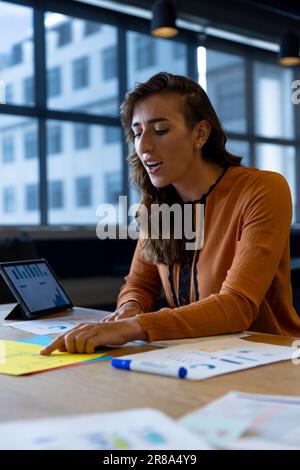 Caucasian casual businesswoman talking and reading document during video call at desk in office Stock Photo