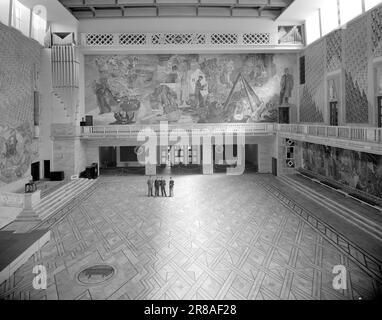 Current 14-1950: Norway's modern representation building. City Hall in Oslo. This is the hall seen from the main entrance. The short wall above the entrance is adorned with Alf Rolfsen's frescoes, a cavalcade of pictures of working life inNorway. Here we find the fisherman with his net, the farmer, the sailor and the lumberjack. Spiritual life is represented by the towering Bjørnson division on the right, the urge to travel by Nansen on the left. The 'wallpaper' decorations on the walls in the hall are also Rolfsen's works. TV one sees the beginning of the wide repo staircase that leads up to Stock Photo