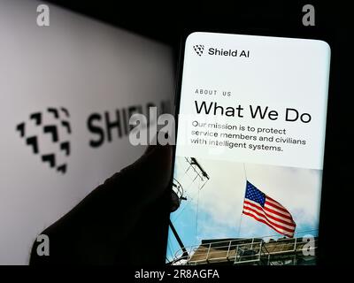 Person holding cellphone with webpage of US aerospace and defense company Shield AI on screen in front of logo. Focus on center of phone display. Stock Photo