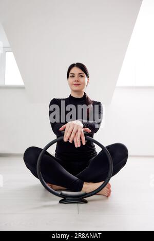 A beautiful young girl is engaged in Pilates in a bright studio. A slender brunette in a black bodysuit does exercises with a spring reformer while si Stock Photo