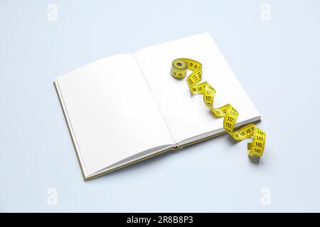 Blank open notebook and measuring tape on light background Stock Photo