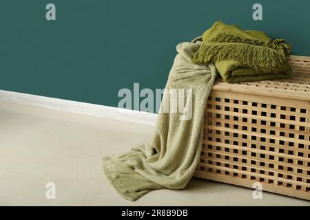New soft blankets on basket near green wall Stock Photo