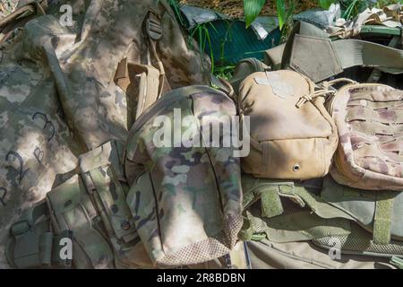 Bag, backpack and body armor of a military man. Old equipment. Outfit. Pixel uniform. Textile green background. A first-aid kit and marching things of a soldier. Stock Photo