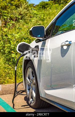 Electric car at charging station with power cable supply plugged in on blurred nature with soft light background. Charging an electric car with the po Stock Photo