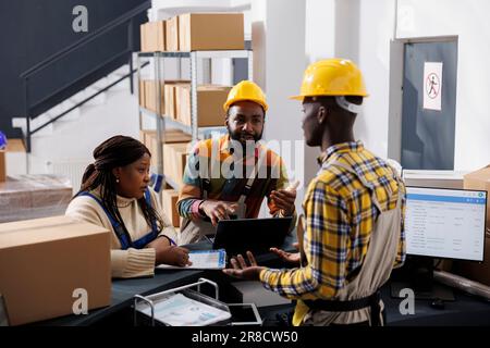 Delivery service workers checking goods inventory on laptop at post office reception counter. African american logistics department managers discussing products supply chain in postal storehouse Stock Photo