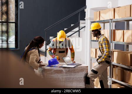 Storehouse employees preparing order and chatting in storage room. African american men and woman shipment managers standing near cardboard boxes shelf while dicussing work in warehouse Stock Photo