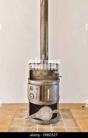 a wood burning stove in the corner of a room with tile floor and white wall behind it is an open door Stock Photo