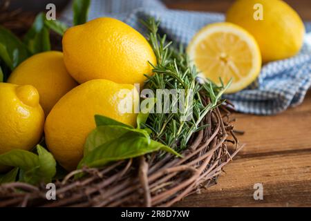 Fresh lemons with rosemary sprigs arranged in grapevine wreath with lemons blurred in background on blue and white towel Stock Photo