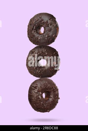 Tasty chocolate donuts falling on pastel violet background Stock Photo