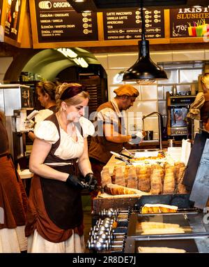 Prague, Bohemia - CZ– June 3, 2023 Woman preparing Trdelnik or Chimney cake. It is made by depositing layers and layers of dough on a cylindrical spit Stock Photo