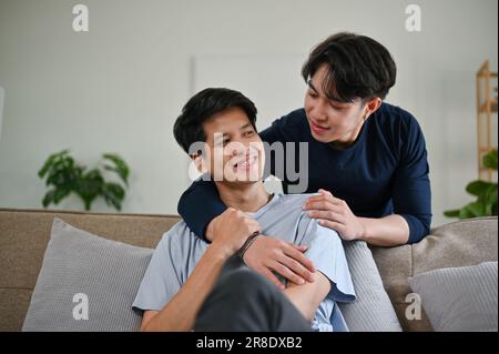 Happy and carefree young Asian male gay couple hugging each other while relaxing in the living room together. LGBTQ+, homosexual, gay couple Stock Photo