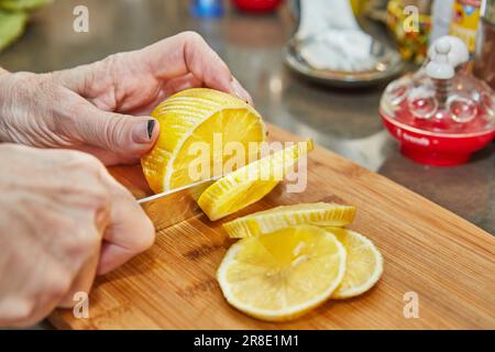 Citrus Zest: Skillful Chef Slices Fresh Lemon Circles on a Rustic Wooden Board in the Vibrant Kitchen. Stock Photo