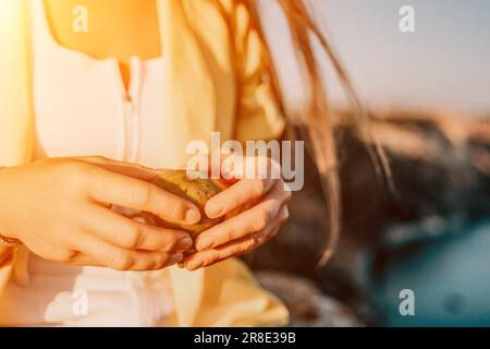 Woman's hands opening a fig to eat. Fresh ripe fig fruit in the hands. A young woman eats figs on the beach, near sea. Ficus carica, Fig - green Stock Photo