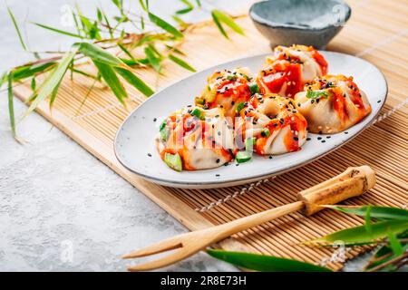 Steamed dumplings Dim Sum with  hot Sriracha sauce and green onions and sesame seeds. Stock Photo