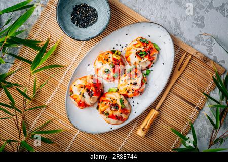 Steamed dumplings Dim Sum with  hot Sriracha sauce and green onions and sesame seeds. Stock Photo