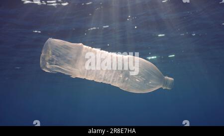Disposable plastic bottle drift under surface of water in bright sunrays. A plastic bottle is thrown into the sea slowly drifts in water column in ray Stock Photo