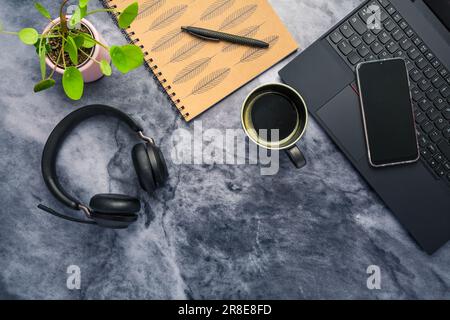 Working from home. Desk office with laptop, notepad, coffee cup,  headphones and plant Stock Photo