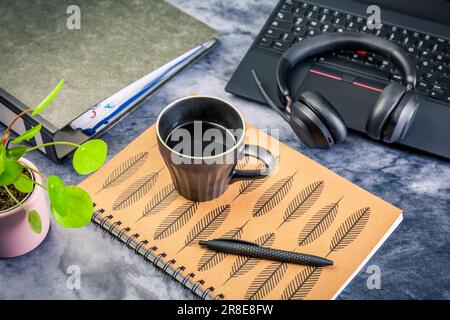 Working from home. Desk office with laptop, notepad, coffee cup,  headphones and plant Stock Photo
