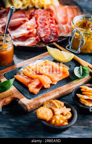 Appetizers with different antipasti, charcuterie, snacks, meat platter with cheese and spicy olives, salmon carpaccio and tomato salad Stock Photo