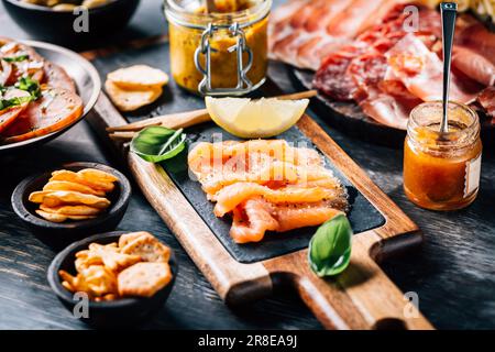 Appetizers with different antipasti, charcuterie, snacks, meat platter with cheese and spicy olives, salmon carpaccio and tomato salad Stock Photo