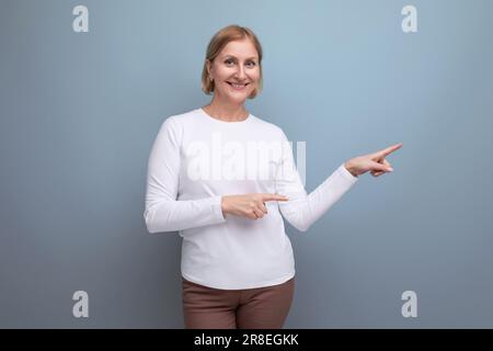 happy healthy blonde middle aged woman in a white sweater in the premenopausal phase points her finger to the side Stock Photo