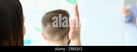 Young woman raising hand to ask question at indoor business training closeup Stock Photo