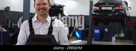 Smiling young mechanic writes on clipboard, machines in background. Mechanic in repair shop takes order for auto maintenance Stock Photo