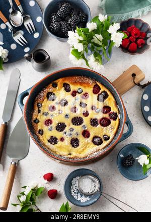 Delicious blackberry, raspberry clafoutis in a blue ceramic baking pan with icing sugar on wooden board. Homemade sweet food. Top view. Stock Photo