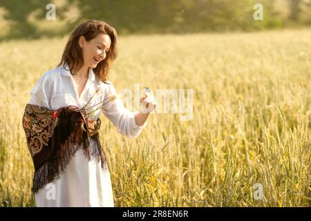 a young white woman went for a walk in a wheat field in the early summer morning,  a blue butterfly landed on her finger, the girl was very surprised. Stock Photo