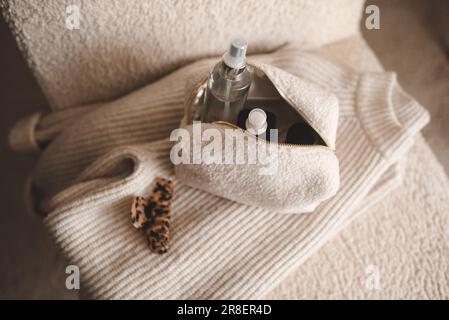 Fluffy cosmetic bag with make up cosmetic products on knitted clothes in chair closeup top view. Stock Photo