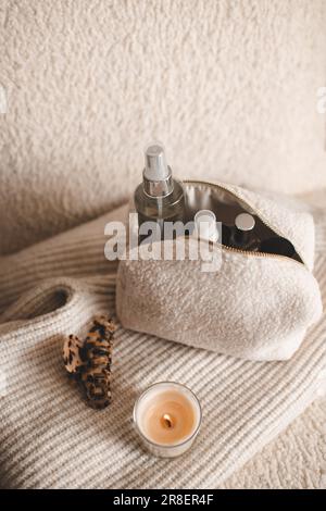 Fluffy cosmetic bag with make up cosmetic products and scented candle on knitted clothes in chair closeup top view. Stock Photo